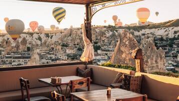 Une terrasse dotée de mobilier en bois et offrant une vue sur une ville où l’on peut admirer des montgolfières.