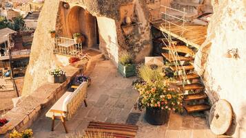 A rooftop terrace with stone walls, a wooden bench, potted plants, and a view of the city.