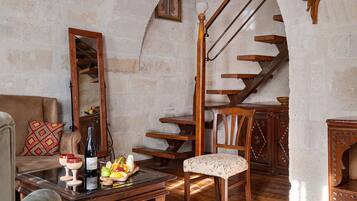 Un interior rústico con una escalera de madera, una mesa de comedor dispuesta con vino y fruta, y una zona de estar acogedora.