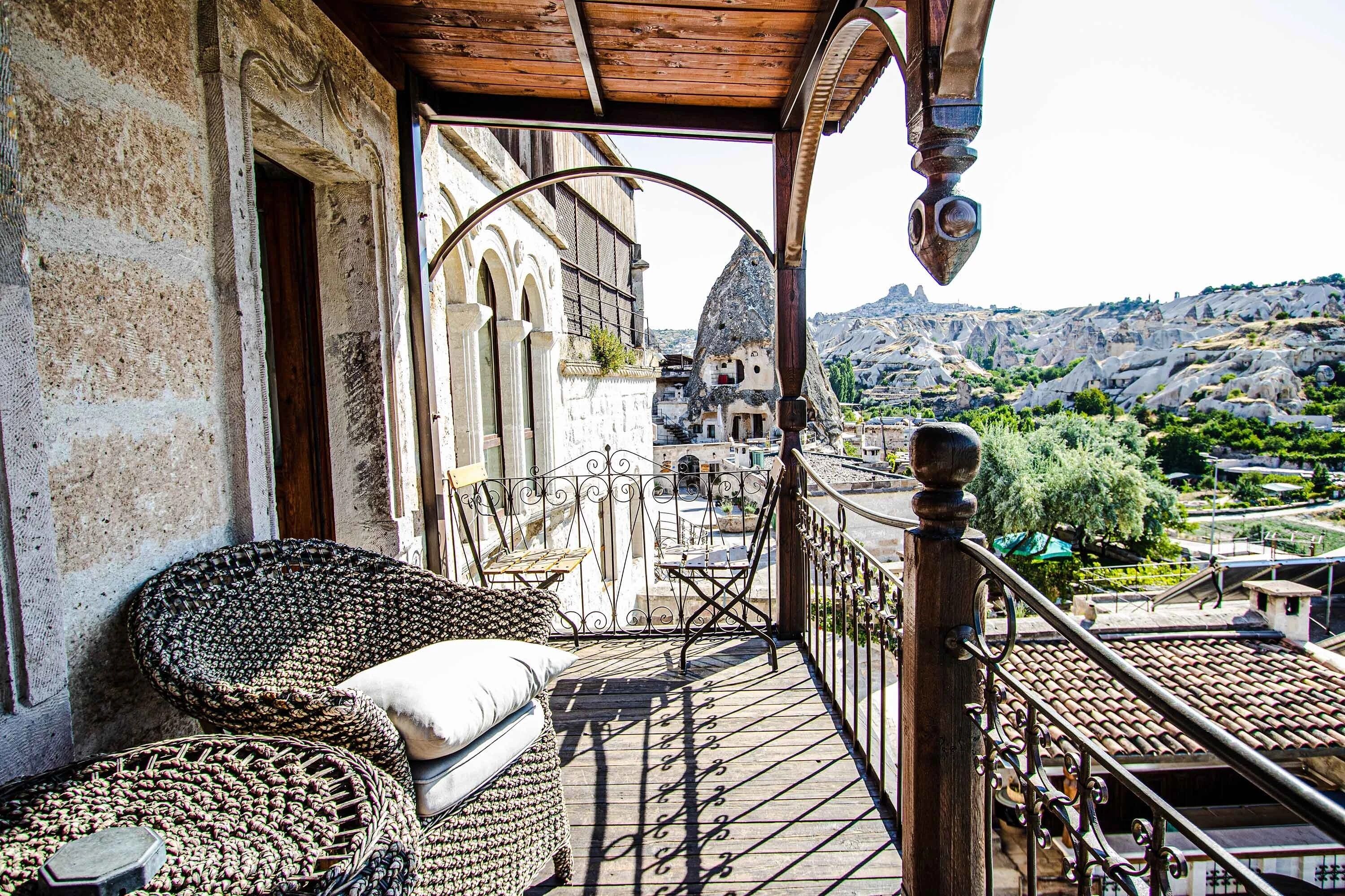 A balcony with wicker furniture, a view of a traditional building, and a mountainous landscape.
