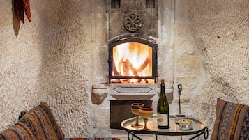 Une pièce chaleureuse avec une cheminée en pierre, deux canapés à motifs, une petite table avec une bouteille et des verres, et un tapis en fourrure.