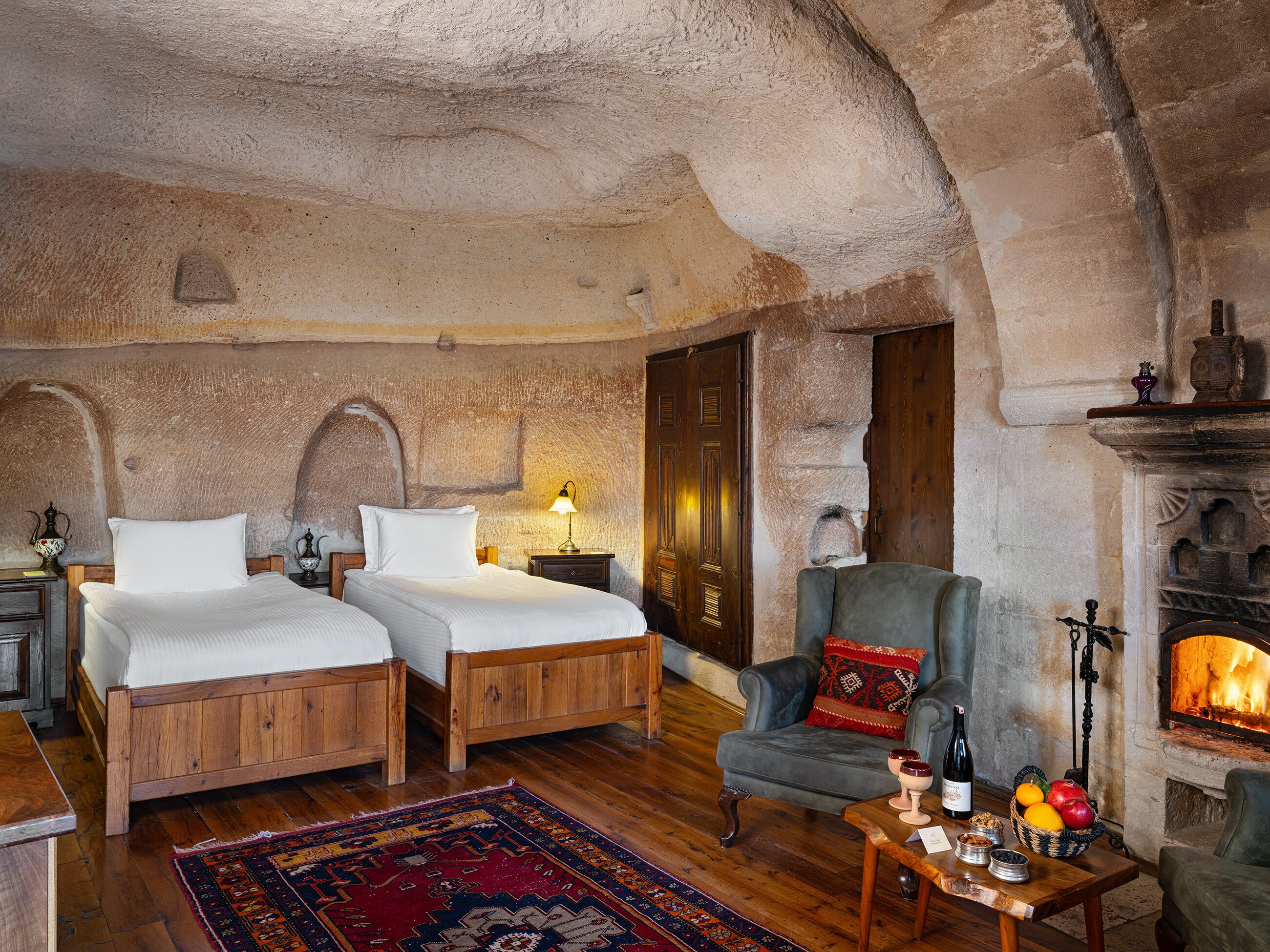 A rustic room with two wooden beds, a stone fireplace, and a traditional armchair.