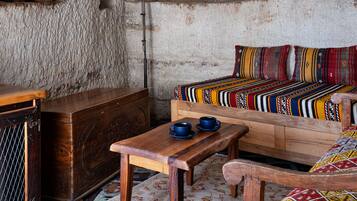 A rustic room with a stone wall, a wooden table, a sofa with colorful cushions, and a metal lamp.