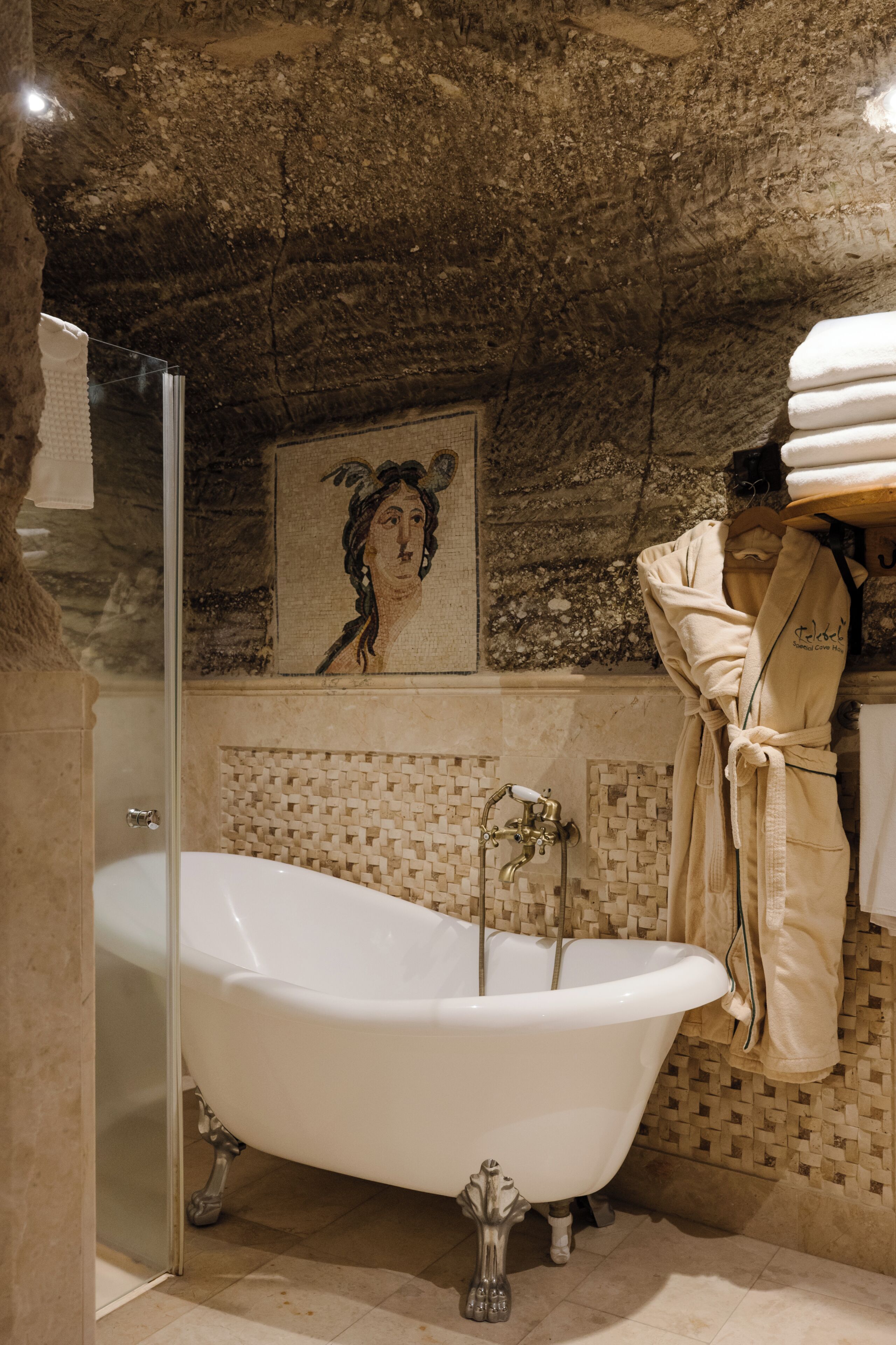 A bathroom with a clawfoot bathtub, a glass shower enclosure, and a mosaic wall.