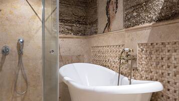 Un baño con una bañera independiente, ducha con cerramiento de vidrio y pared con mosaicos.