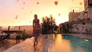 A pool area with a view of the sunset and hot air balloons in the sky.