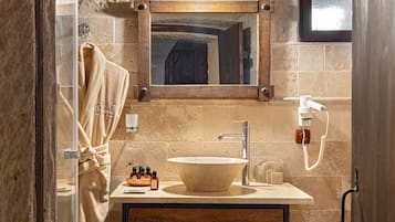 A rustic bathroom with a stone wall, wooden beams, a large mirror, a wooden vanity, a white sink, and a toilet.