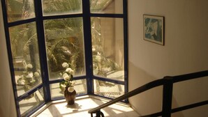Una habitación de esquina con un ventanal grande, una pequeña mesa con un florero y una escalera.