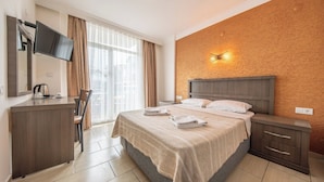 Habitación de hotel con cama, escritorio con hervidor, televisión y lámpara fijada a la pared.