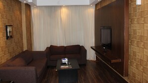 A modern living room with a brown sofa, a black coffee table, and a flat-screen TV mounted on a wooden wall. - Terrace Furnished Apartments Fintas 2 (Fintas)
