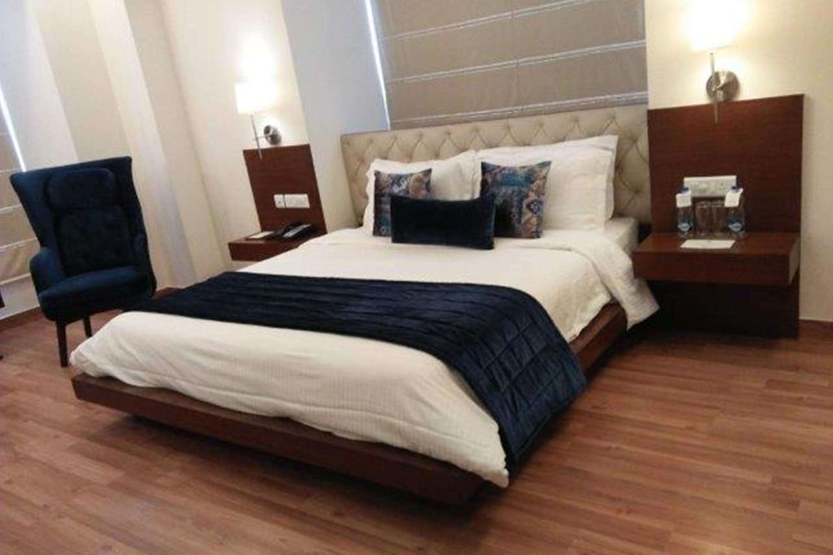 Una habitación de hotel con una cama grande, una silla, una mesita de noche y una mesita auxiliar.