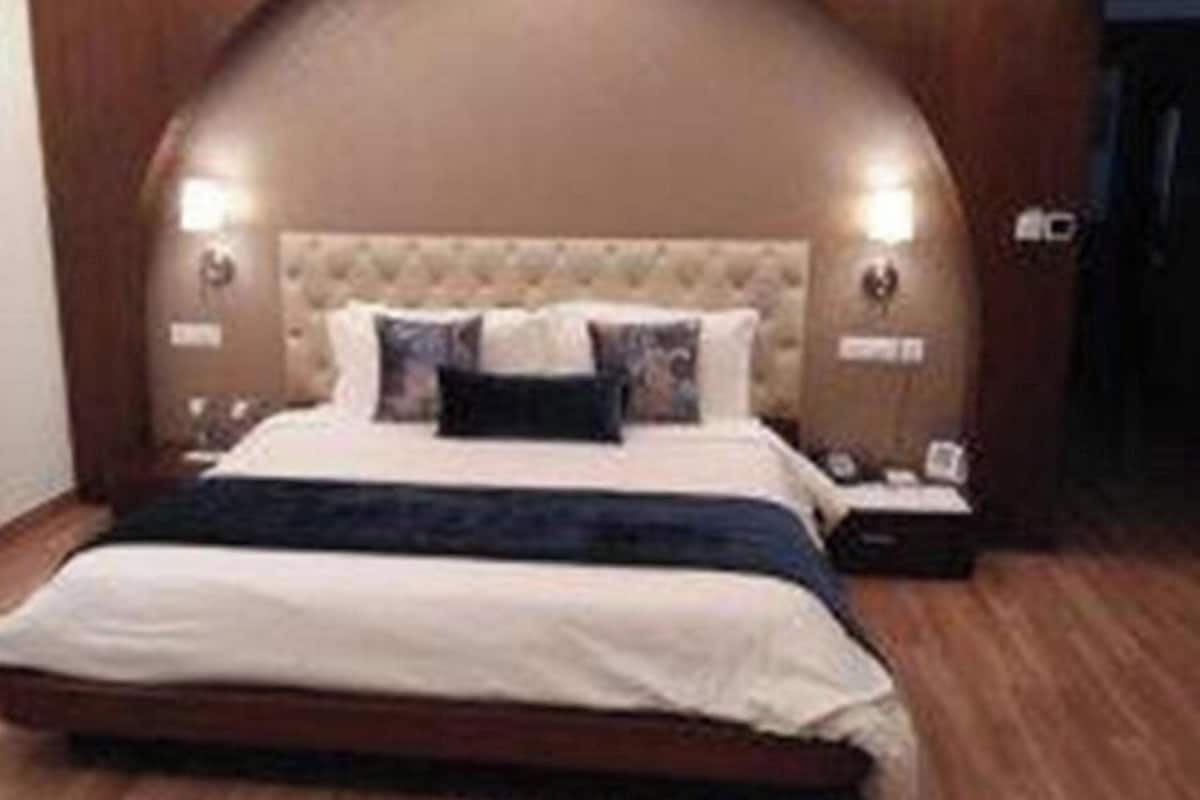 A bedroom with a tufted headboard, a bed with white bedding and a dark throw, two bedside lamps, and a wooden floor.