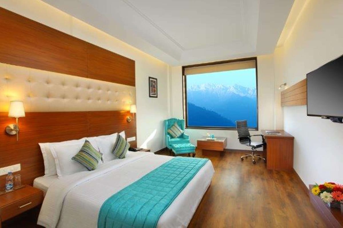 Habitación de hotel con una cama grande, un escritorio, una silla, un televisor y una ventana con vistas a la montaña.
