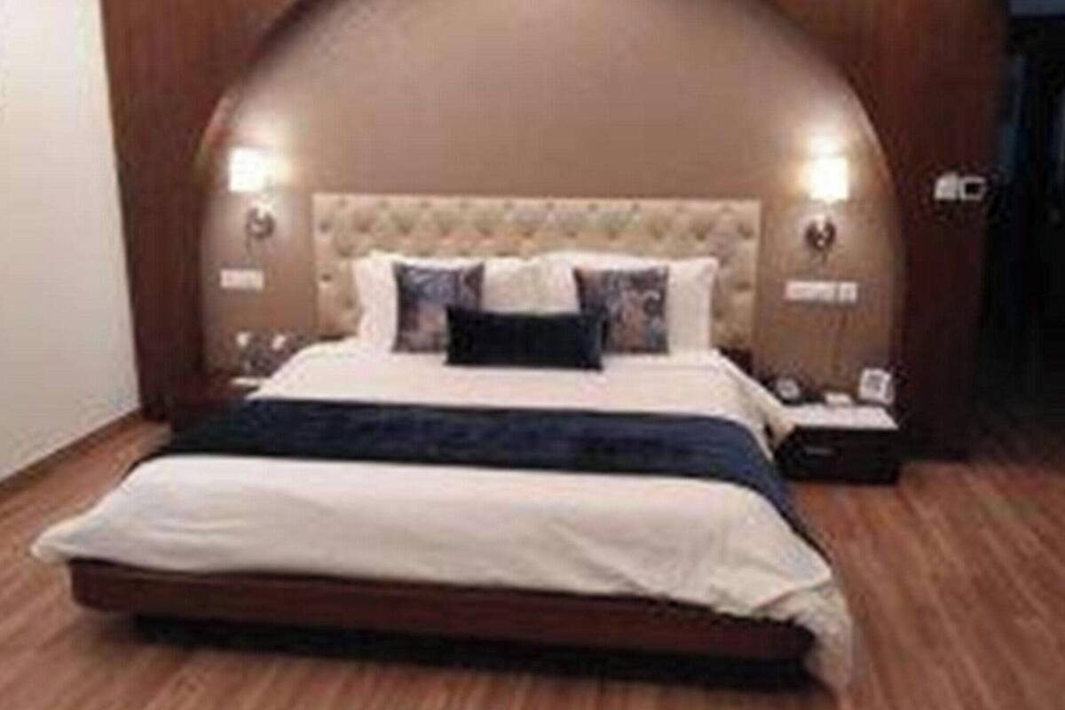 Ein Schlafzimmer mit einer gepolsterten Kopfstütze, einem Bett mit weißer Bettwäsche und einer dunklen Tagesdecke, zwei Nachttischlampen und einem Holzboden.