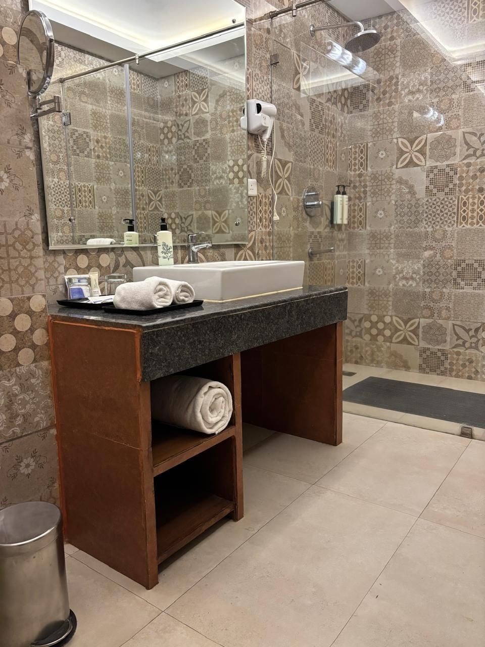 A bathroom with a large mirror, a sink, a shower, and patterned tiles.