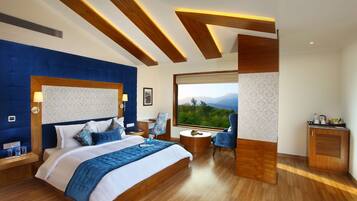 A modern hotel room with a large bed, a desk, and a view of the mountains.