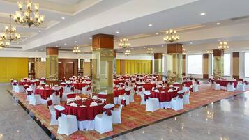 A large banquet hall with round tables covered in red tablecloths and white chairs, arranged in rows.