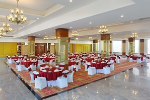 A large banquet hall with round tables covered in red tablecloths and white chairs, arranged in rows.