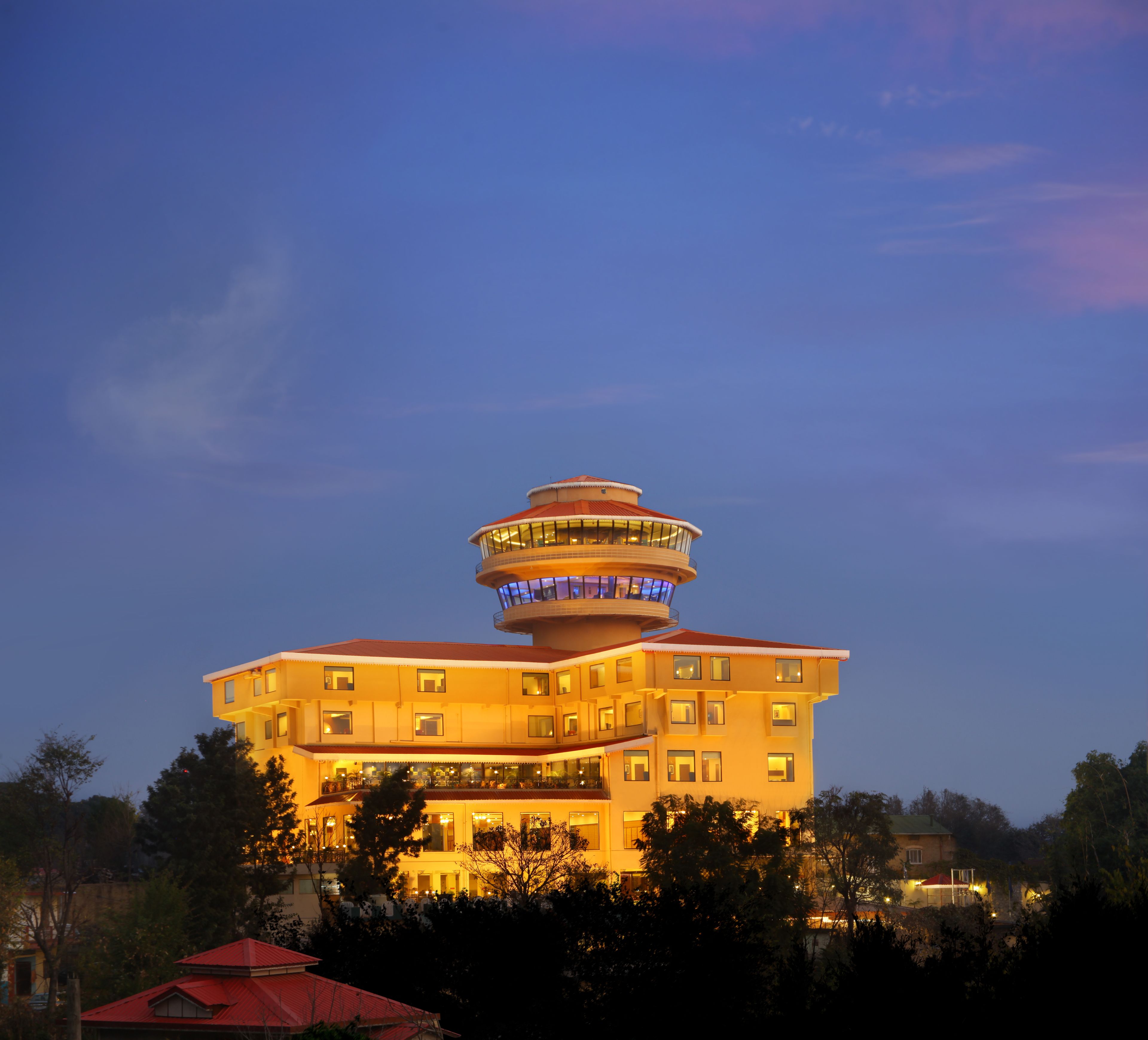 A multi-story hotel with a distinctive tower-like structure on the roof, surrounded by trees.