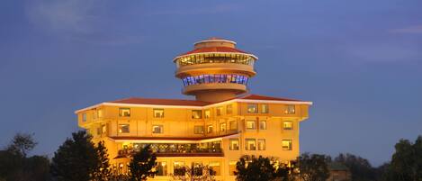 A multi-story hotel with a distinctive tower-like structure on the roof, surrounded by trees.