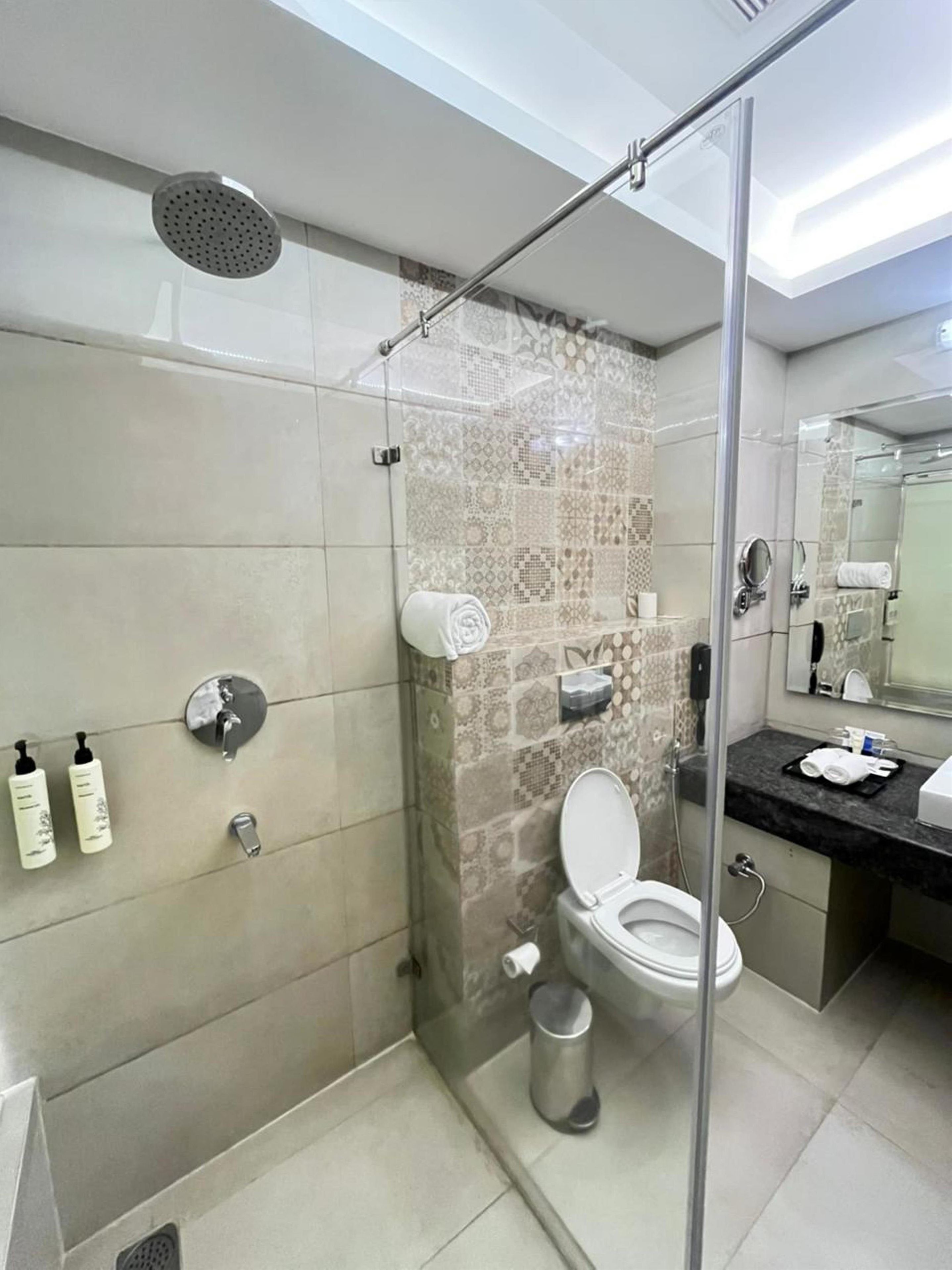 A modern bathroom with a glass-enclosed shower, a toilet, and a sink with a mirror.