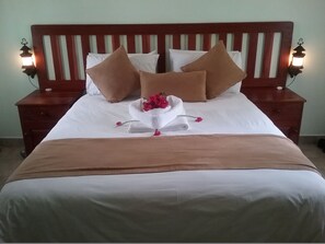Una cama bien hecha con una colcha marrón, sábanas blancas y varias almohadas. Hay dos mesitas de noche con lámparas a cada lado de la cama.
