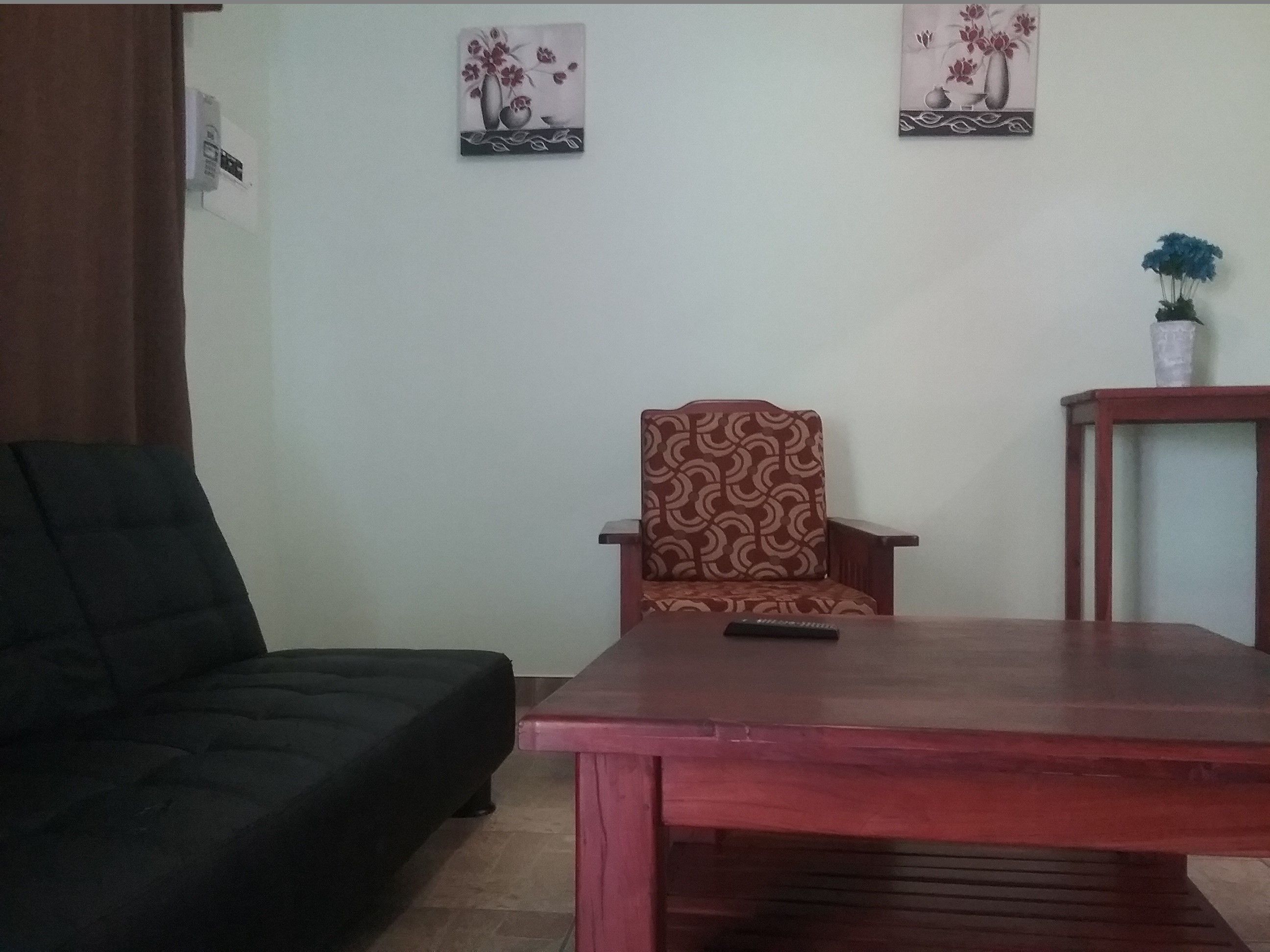 A living room with a dark-colored sofa, a patterned armchair, a wooden coffee table, and two wall-mounted paintings.