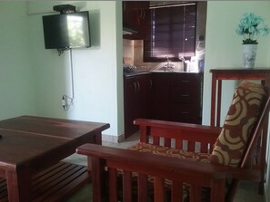Una sala de estar con una mesa de comedor de madera y un sillón estampado. Un televisor está montado en la pared.