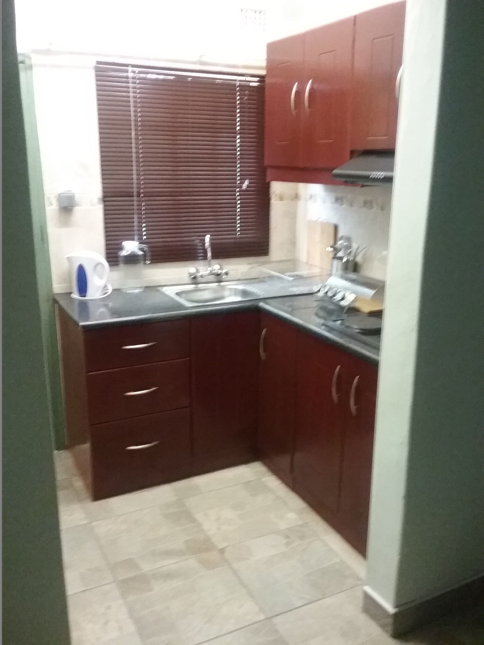 Una cocina compacta con armarios de madera oscura, un lavamanos de acero inoxidable y salpicadero de azulejos.