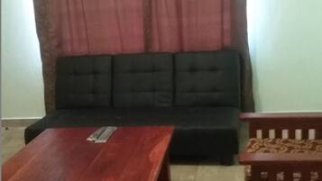 A living room with a black sofa, a wooden coffee table, and a patterned wooden chair.