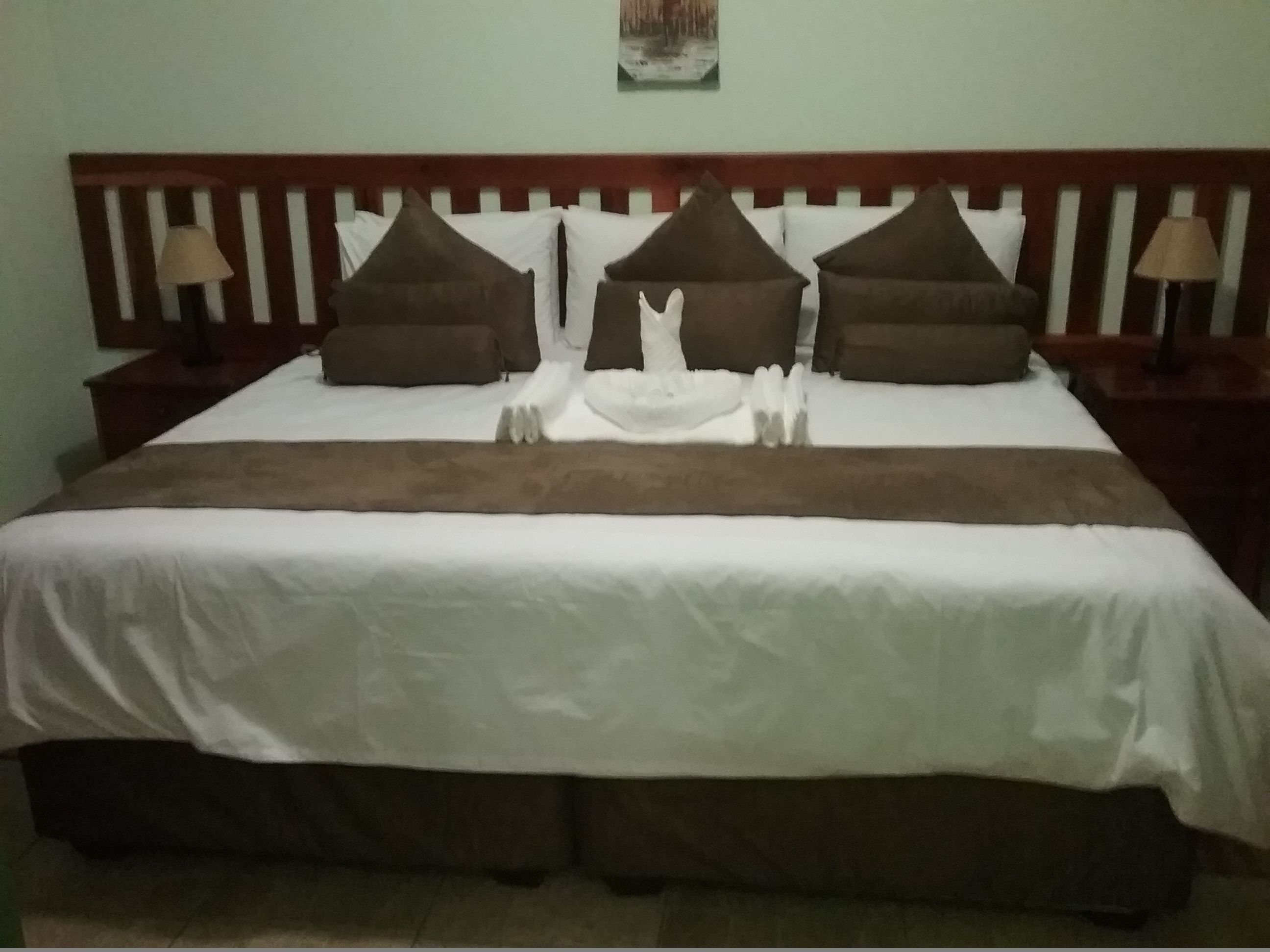 A neatly made bed with white and brown bedding, a wooden headboard, and two bedside lamps.