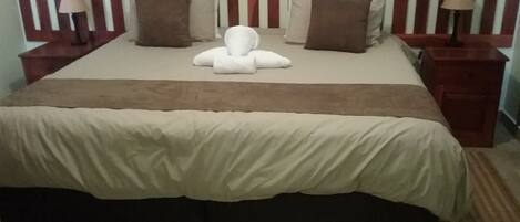 A neatly made bed with a wooden headboard, two bedside tables with lamps, and a brown throw blanket.