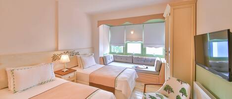 Ein Hotelzimmer mit zwei Betten, einer Sitzecke mit Blick, einem Fernseher und einem Sessel mit Baummuster.