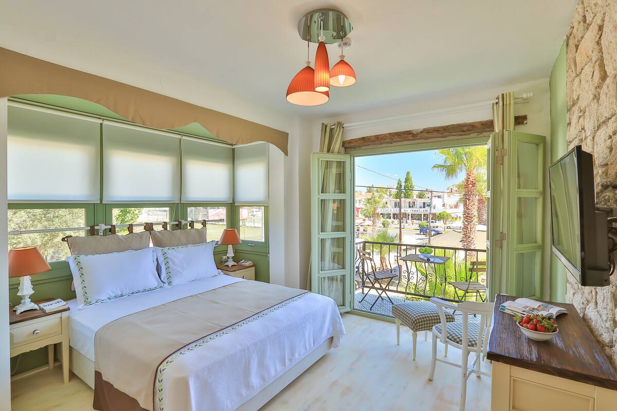 A bedroom with a bed, bedside tables, a balcony with a table and chairs, and a view of the outside.