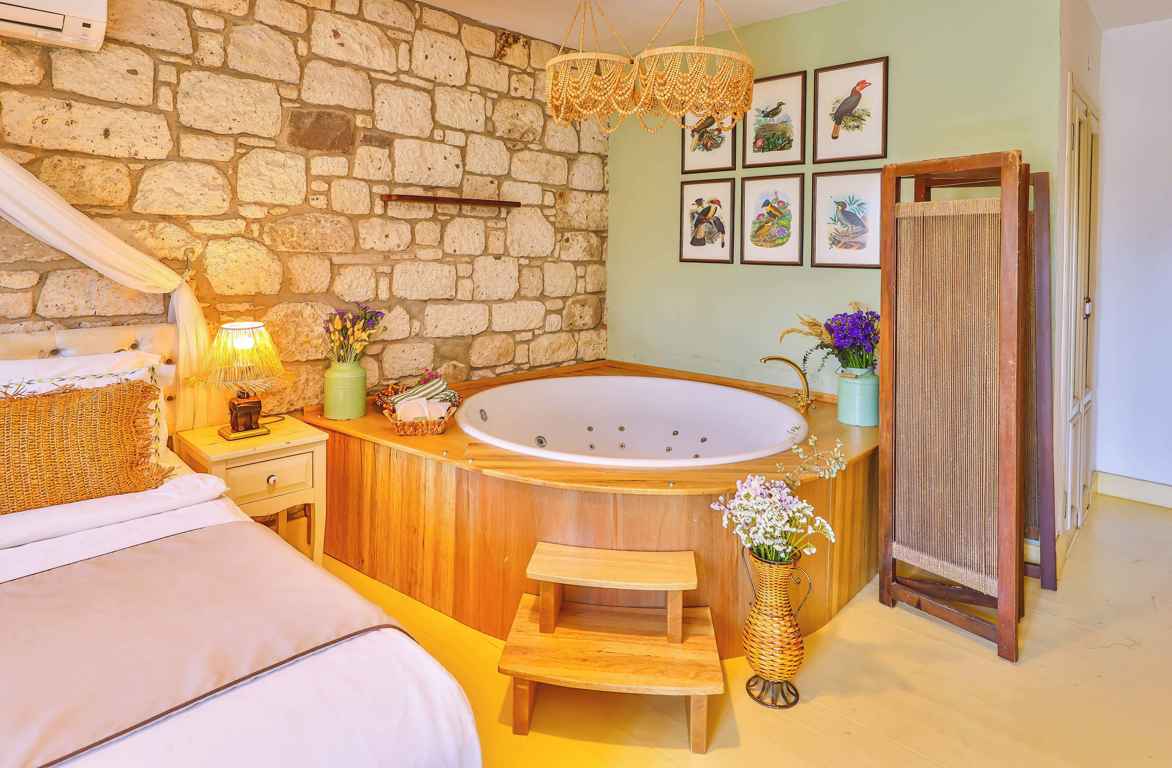 Una habitación con pared de piedra, una bañera de madera, cama con dosel y cuadros enmarcados en la pared.