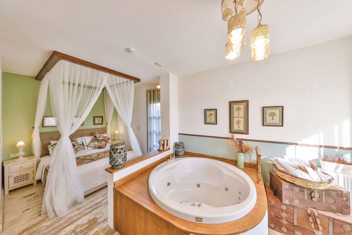A bedroom with a canopy bed, a large bathtub, and a vanity with a mirror.