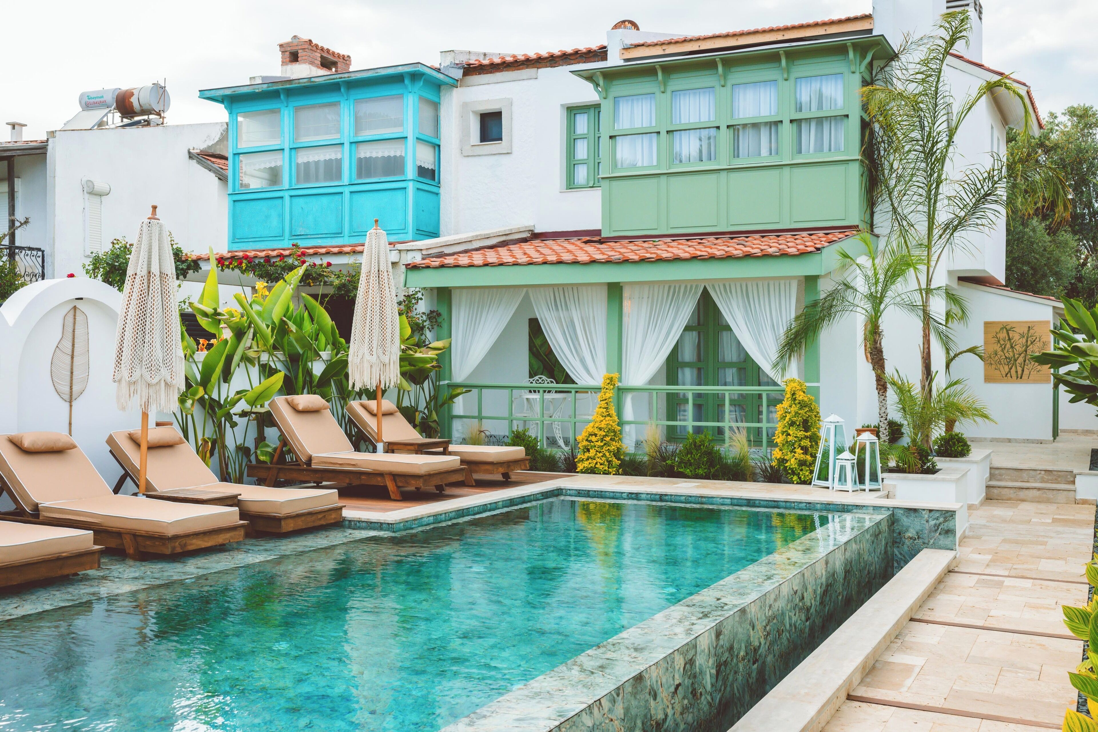 A swimming pool with lounge chairs, a white building with blue and green accents, and tropical plants.