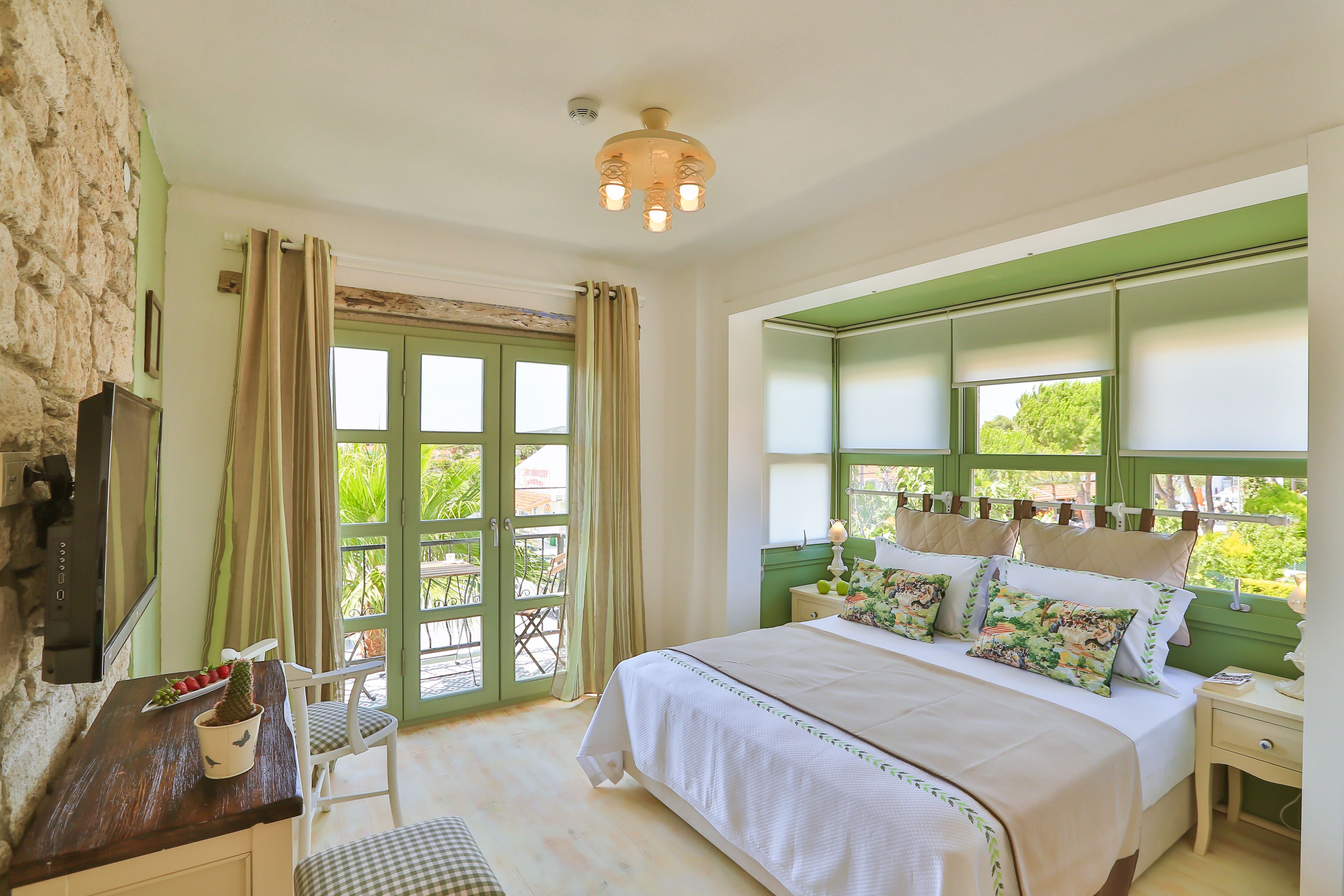 Un dormitorio con cama, escritorio, silla, ventana con cortinas y vista a zonas verdes.