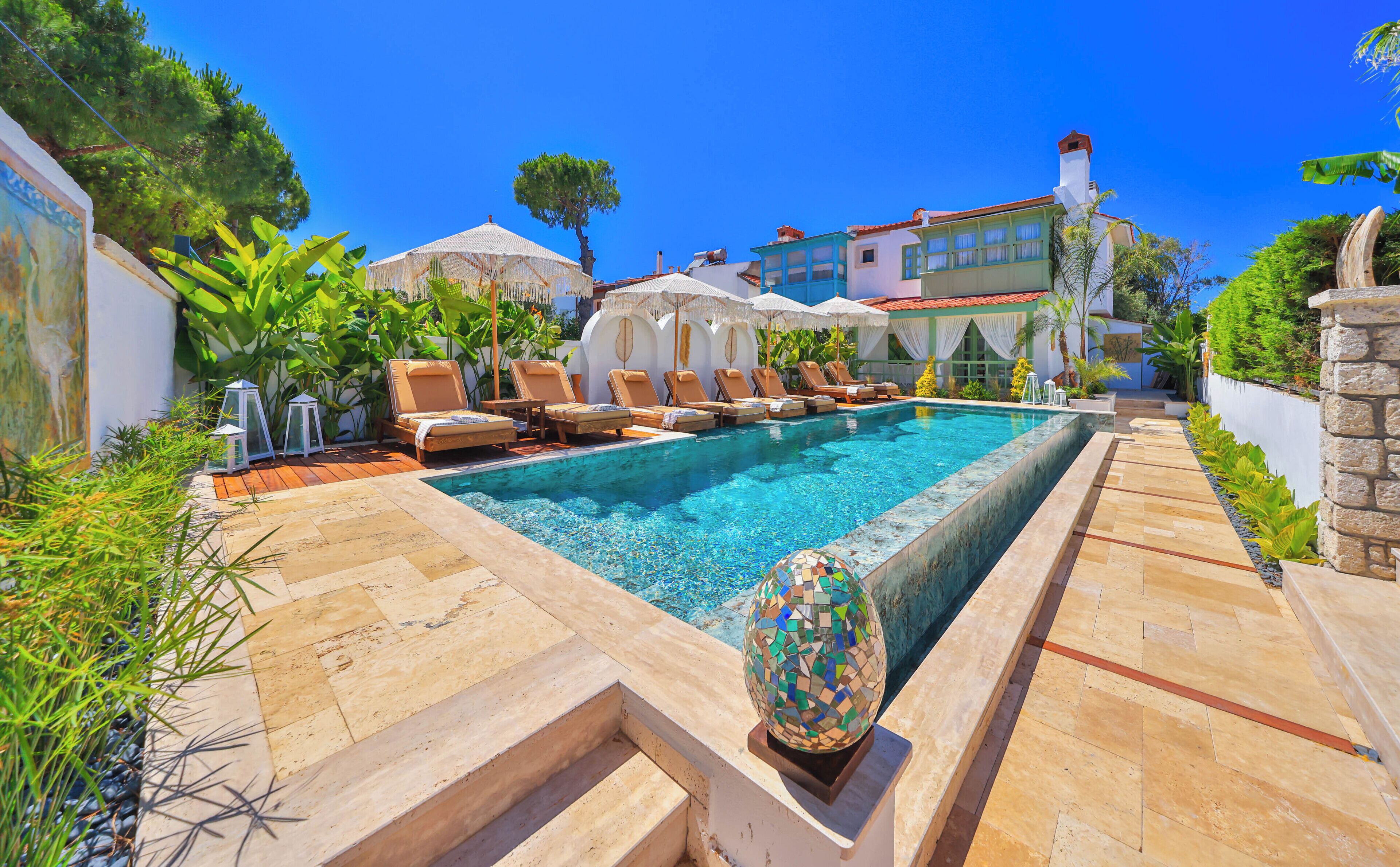 A swimming pool with lounge chairs, a mosaic sculpture, and a building with a red roof in the background.