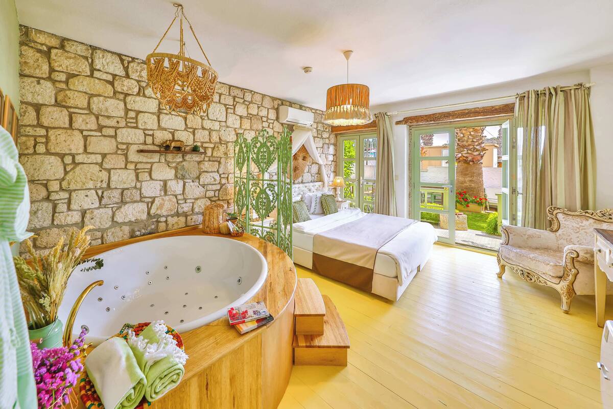 A room with a stone wall, a large bathtub, a bed, and a view of the garden.
