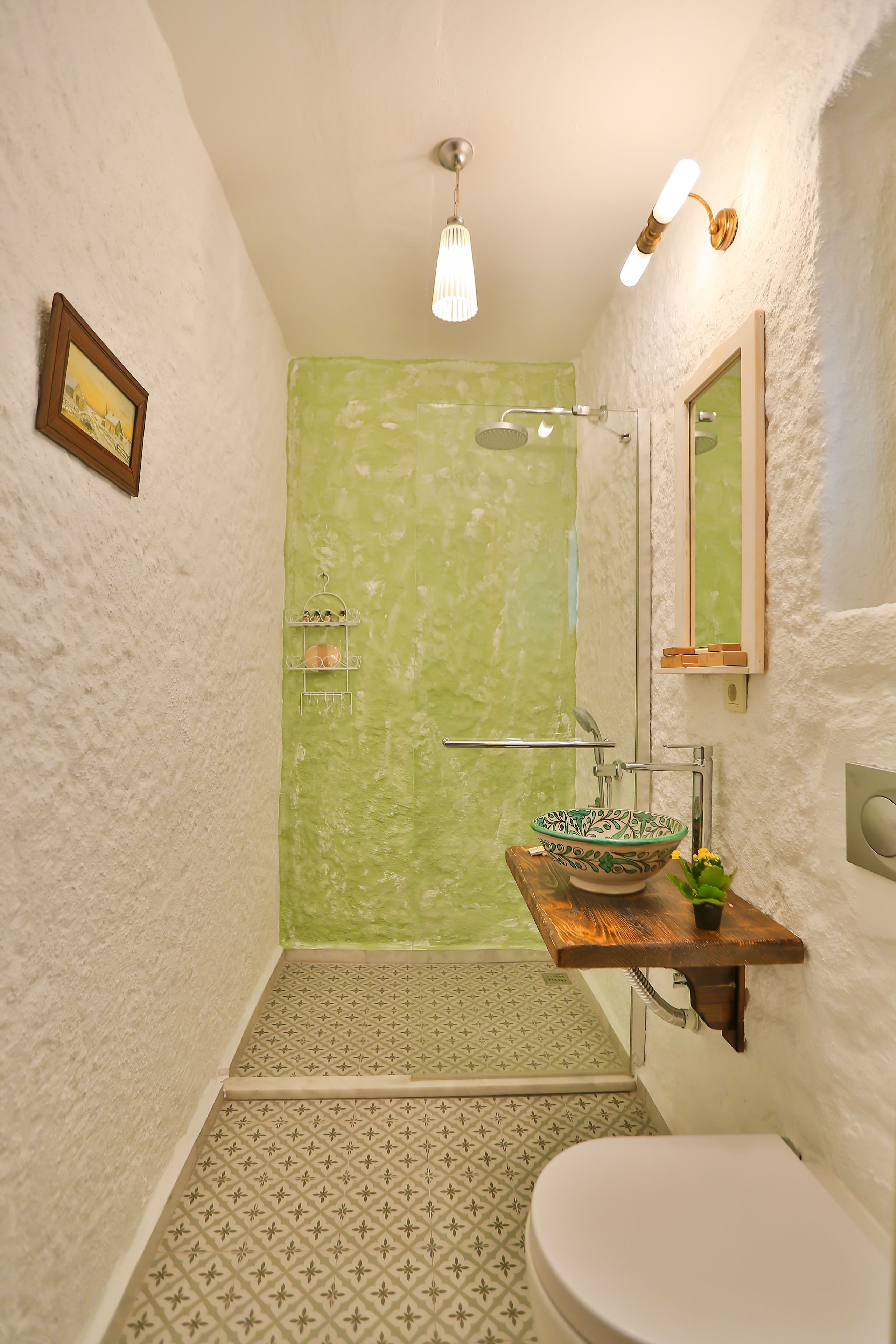 A bathroom with a green shower wall, a white toilet, a wooden sink vanity, and a patterned floor.