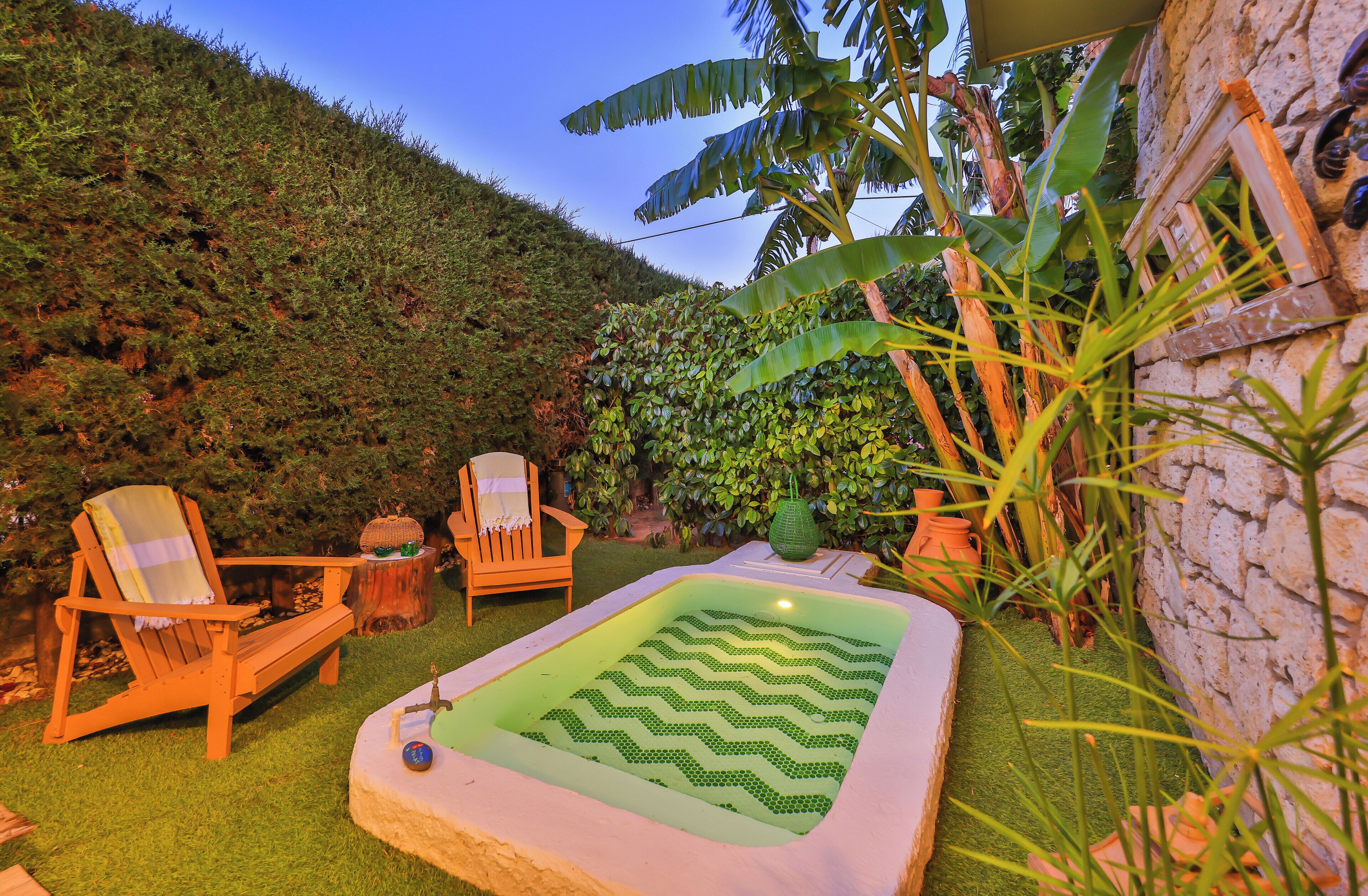 Un jardín con jacuzzi, sillas de madera y un muro de piedra.
