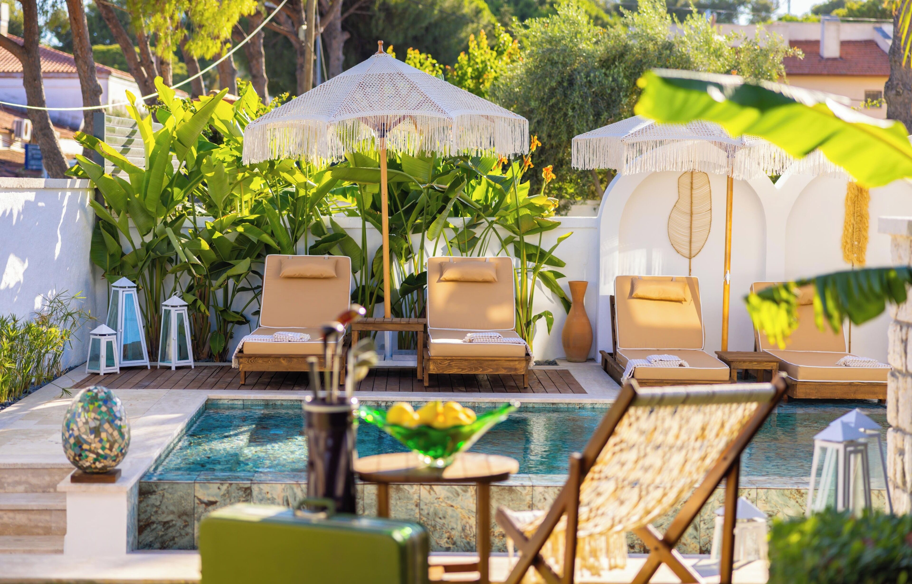 Zona de piscina amb gandules, una taula petita i ombrel·les decoratives.