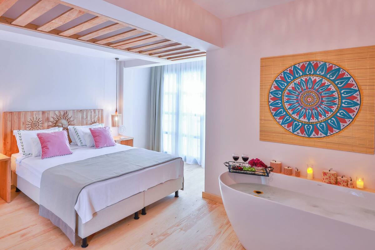 A modern bedroom with a large bed, wooden headboard, bedside lamps, and a wall-mounted artwork.