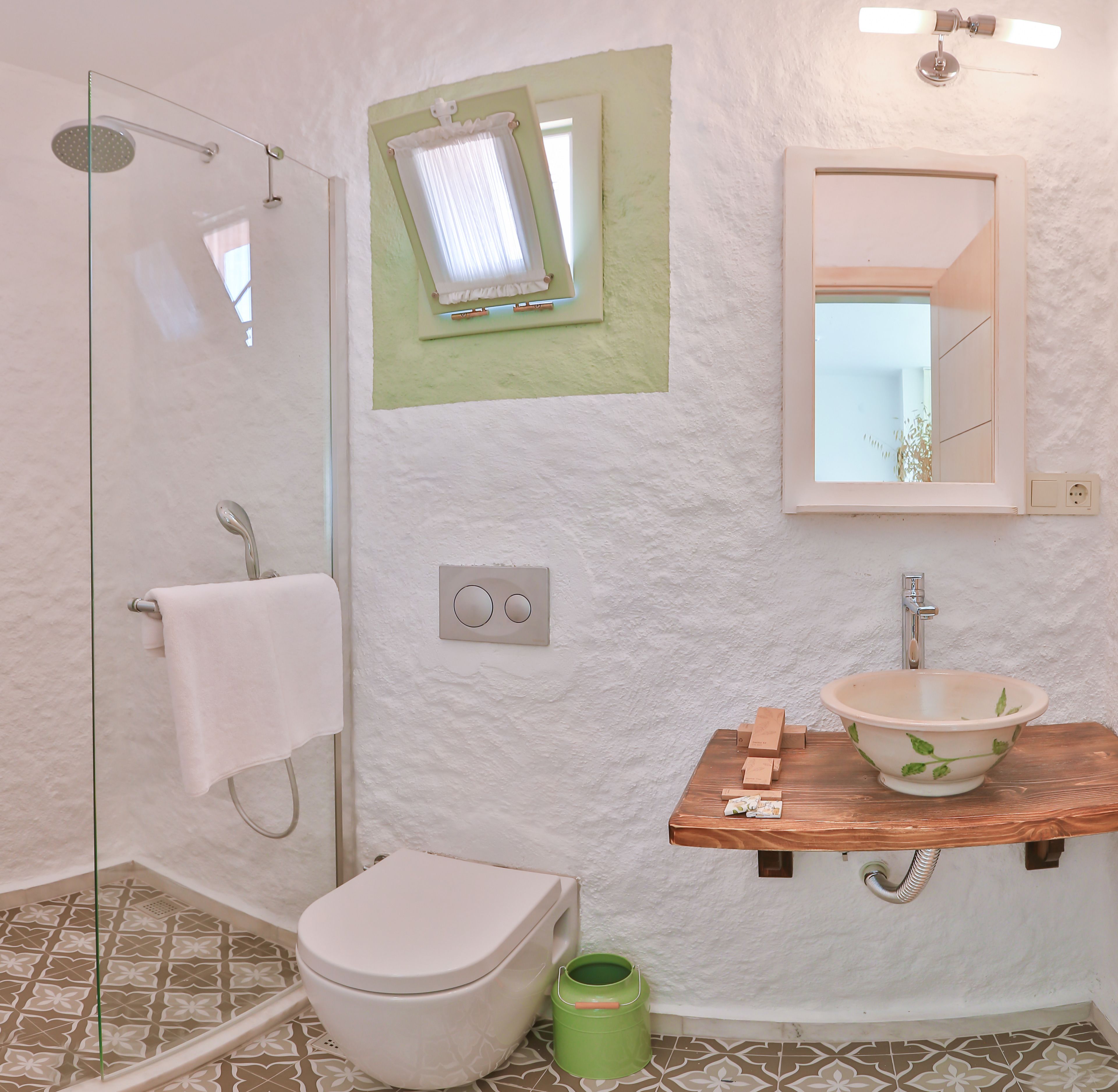 A bathroom with a glass shower enclosure, a toilet, a sink with a wooden countertop, and a mirror above the sink.