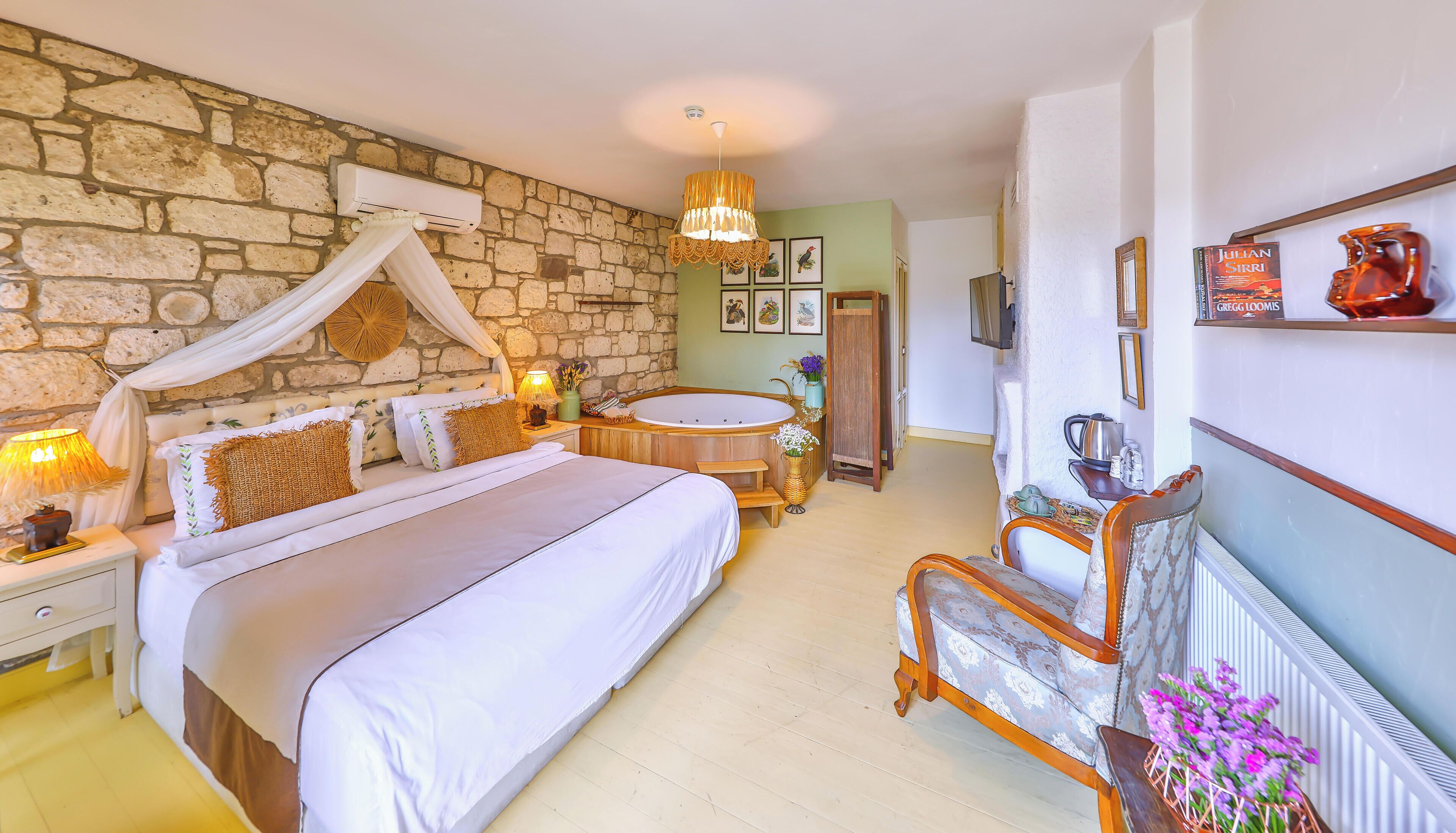 A bedroom with a stone wall, a large bed with a canopy, a wooden bench, a bathtub, and a shelf with decorative items.