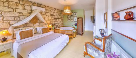 A bedroom with a stone wall, a large bed with a canopy, a wooden bench, a bathtub, and a shelf with decorative items.