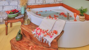 Une salle de bain avec un mur en pierre, une baignoire, un banc en bois et une petite table sur laquelle se trouvent un vase et des fleurs.