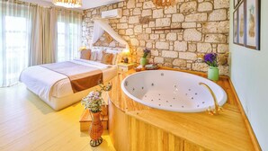 Une chambre avec un mur en pierre, un grand lit, une coiffeuse en bois avec une baignoire et un luminaire suspendu.