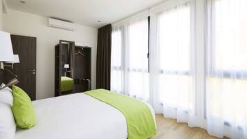 A hotel room with a bed, a wardrobe, a mirror, and a window with sheer curtains.
